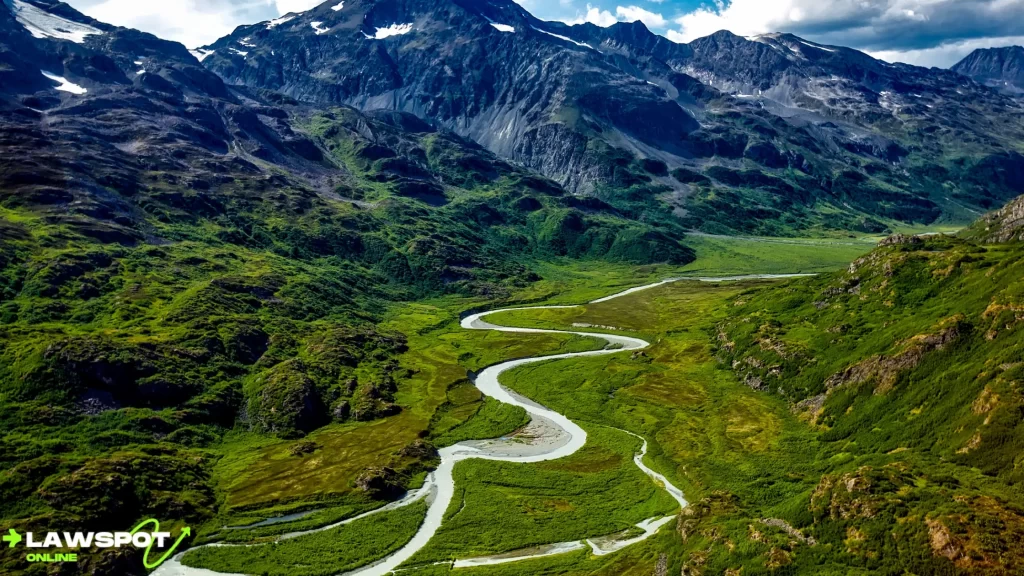 A winding river flows through lush green valleys, surrounded by towering mountains in Alaska’s wilderness. Can you drive to Alaska? Yes, and you’ll be greeted by stunning natural landscapes like this along your journey.